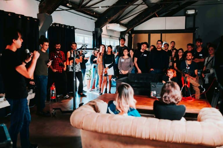 People gathered in a modern indoor space for a presentation or event with a speaker holding a microphone.