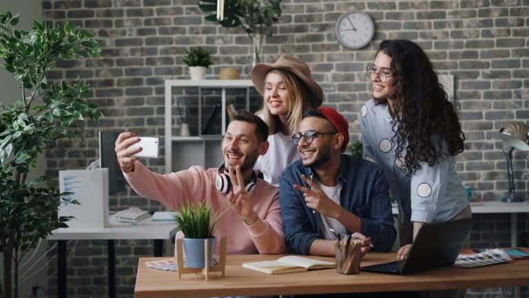 Bright group of friends taking a selfie together in a modern office with exposed brick walls.