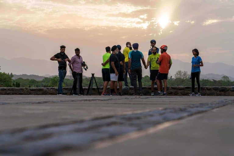 People gathered outdoors during sunset, some with cameras and tripods, enjoying a scenic view with mountains and trees in the background in Perth, Australia.